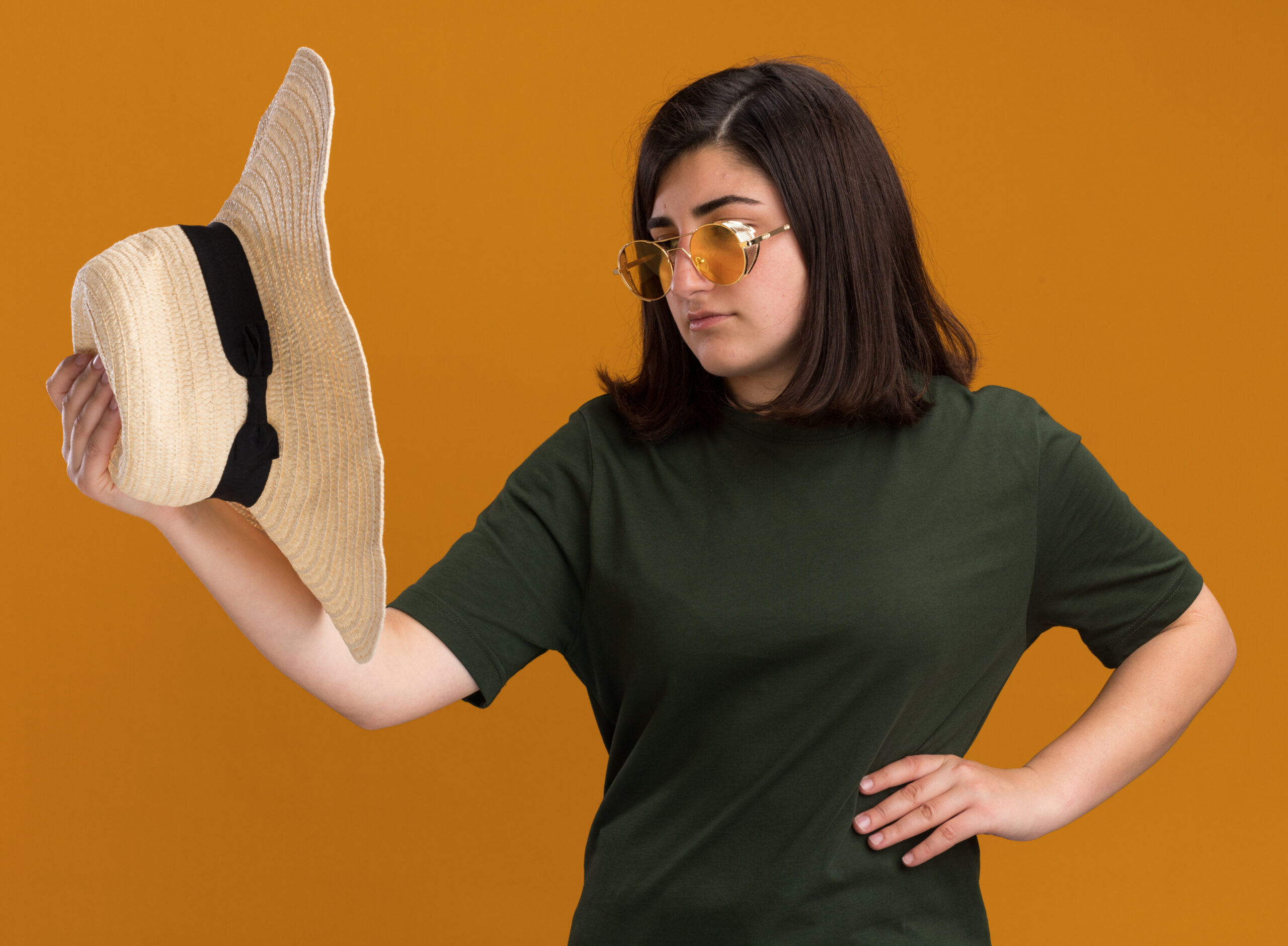 Home Confident Young Pretty Caucasian Girl Sun Glasses Holding Looking Beach Hat Isolated Orange Wall With Copy Space Scaled