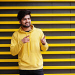 Home Urban Young Hipster Indian Man Fashionable Yellow Sweatshirt Cool South Asian Guy Wear Hoodie Against Striped Background Showing Fingers Free Space 1 150x150