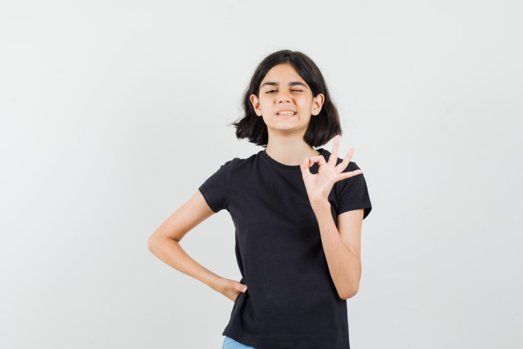 little girl in black t shirt, shorts showing ok gesture, winking eye , front view. little girl in black t shirt, shorts showing ok gesture, winking eye , front view.