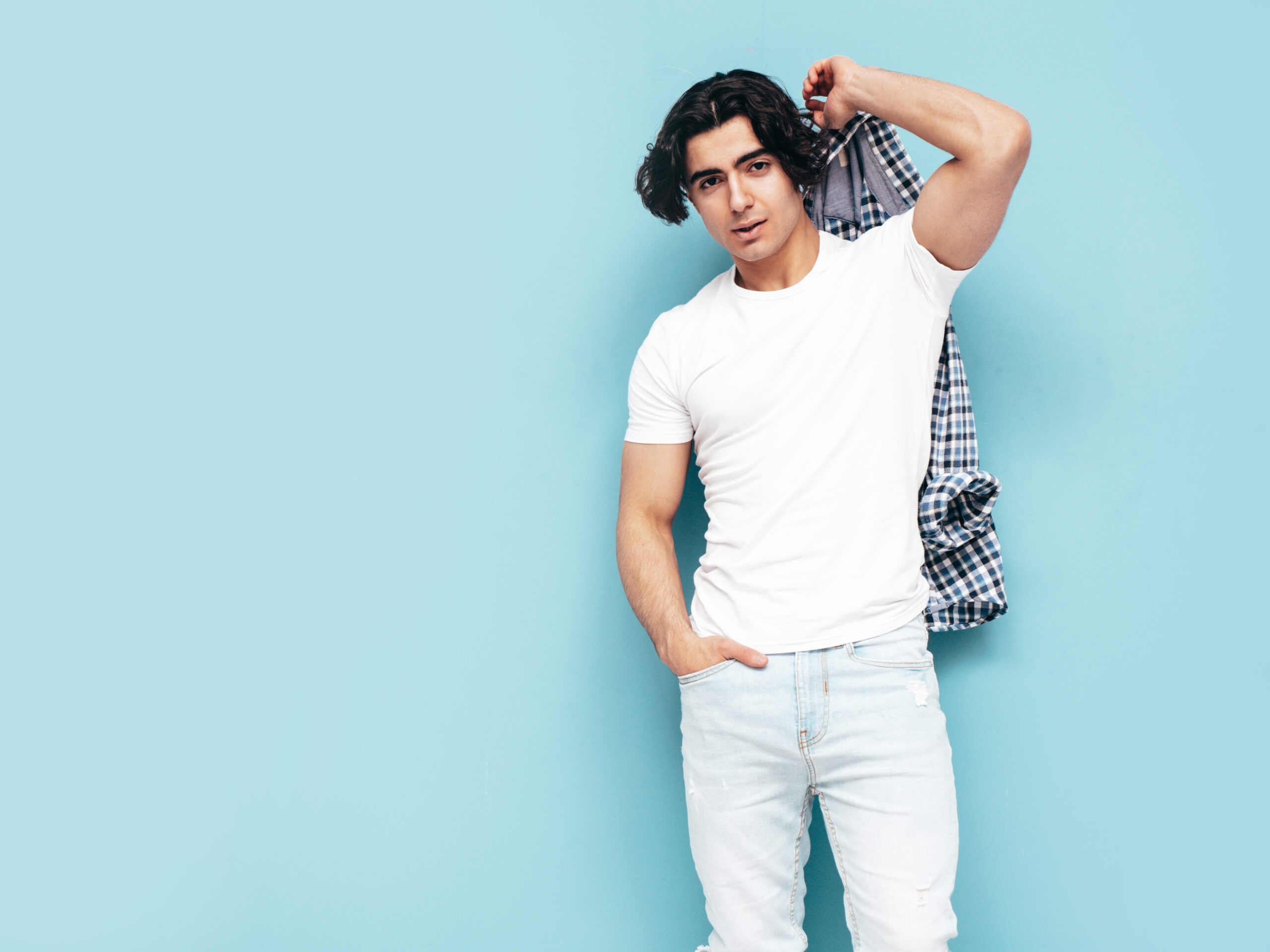 Home portrait of handsome confident model. sexy stylish man dressed in checkered shirt and jeans. fashion hipster male posing near blue wall in studio. isolated